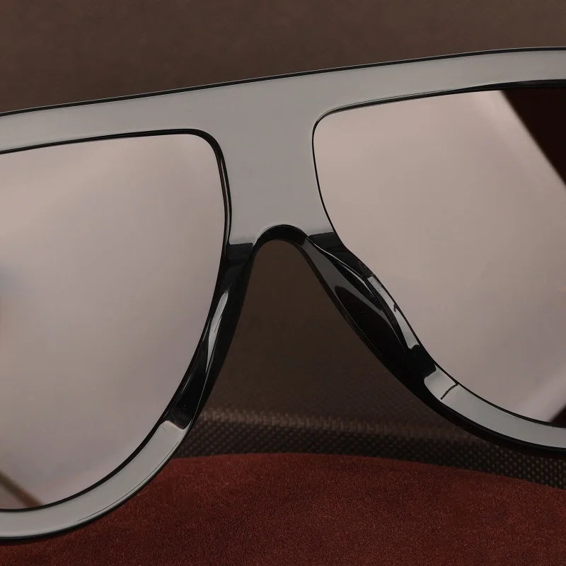 A close-up view of oversized pilot sunglasses with silver frames and light-colored lenses resting on a dark brown surface.