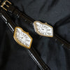 A close-up of a vintage irregular quartz watch with a gold-toned bezel and white face, resting on a black strap.
