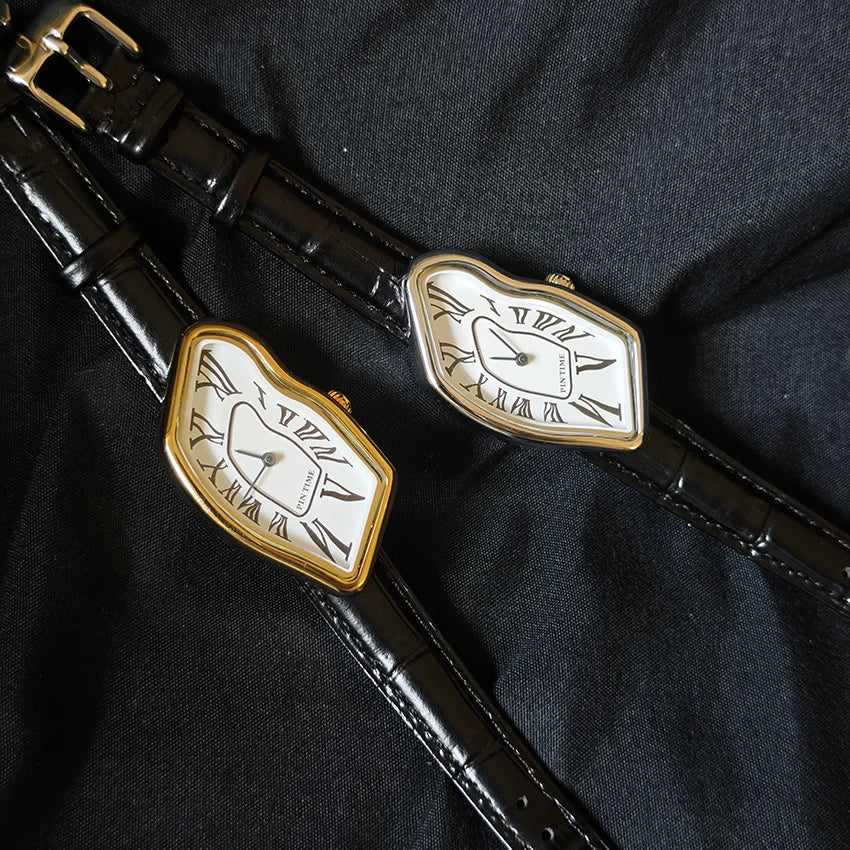 A close-up of a vintage irregular quartz watch with a gold-toned bezel and white face, resting on a black strap.