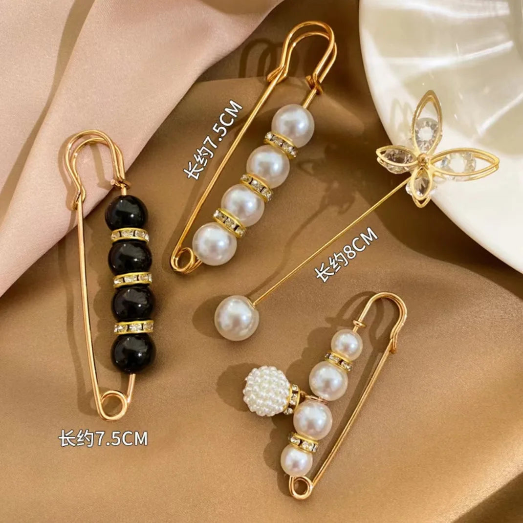 Gold-toned safety pins featuring black and white pearls, including a floral design.