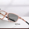 A pair of rose gold photochromic reading glasses with dark lenses resting on a white surface.