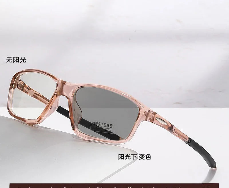 A pair of rose gold photochromic reading glasses with dark lenses resting on a white surface.