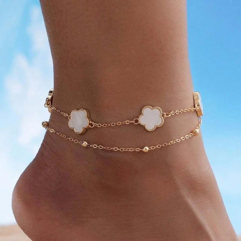 Gold five-leaf clover anklet worn on a person's ankle.