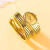 A close-up of a gold quartz watch with an elegant snake design resting on a light yellow background.