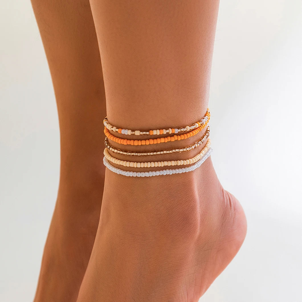 A stack of colorful seed bead anklet bracelets worn on a person's ankle.