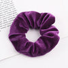 A close-up of a deep purple velvet scrunchie, showing its soft texture and gathered fabric.