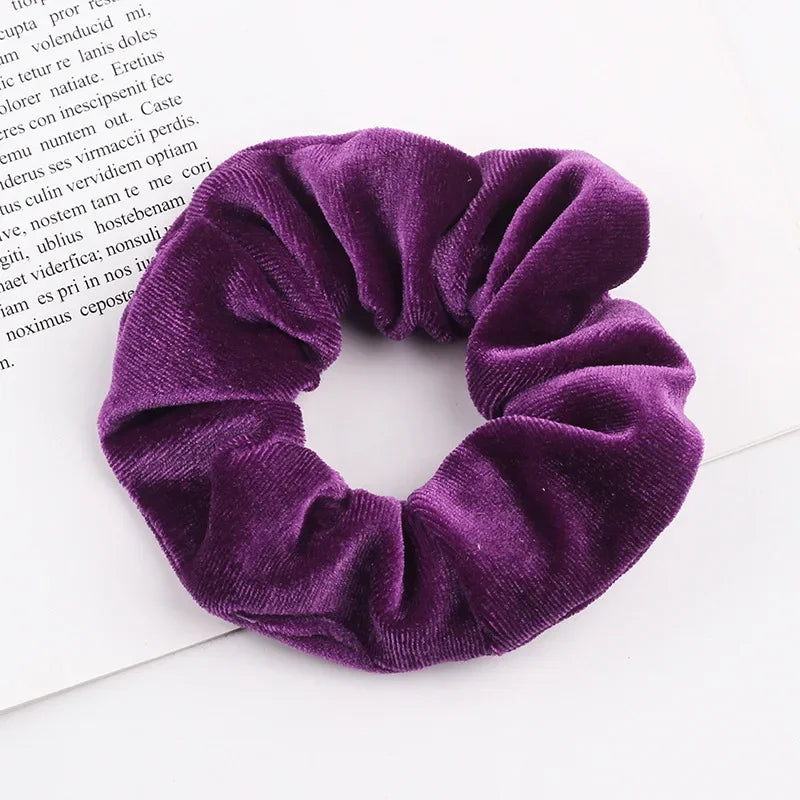 A close-up of a deep purple velvet scrunchie, showing its soft texture and gathered fabric.