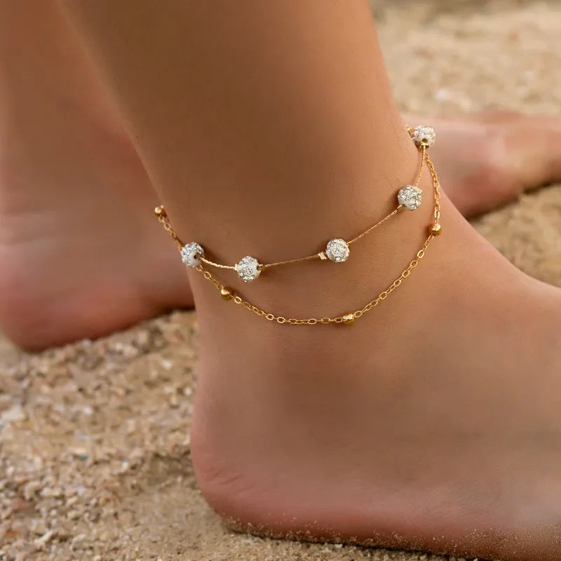 Goldiges Vintage-Schmetterlingsherz-Armband-Set, getragen am Knöchel gegen einen Sandhintergrund