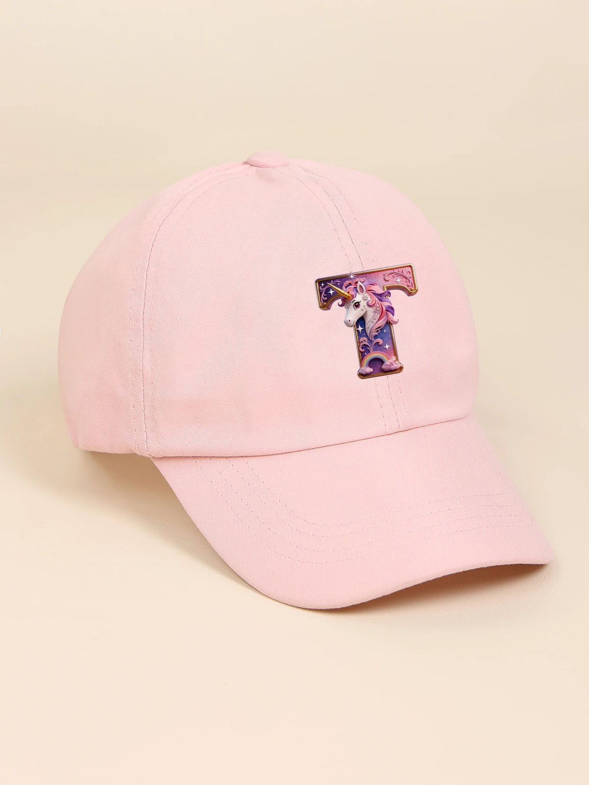 A pink baseball cap featuring a purple and white unicorn letter embroidered on the front.