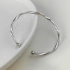 Silver twisted wave cuff bracelet displayed on a white ceramic dish.