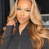 A woman with long, wavy honey blonde hair wearing a black zip-neck top.
