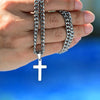 A hand is holding a stainless steel Cuban link necklace with a cross pendant.