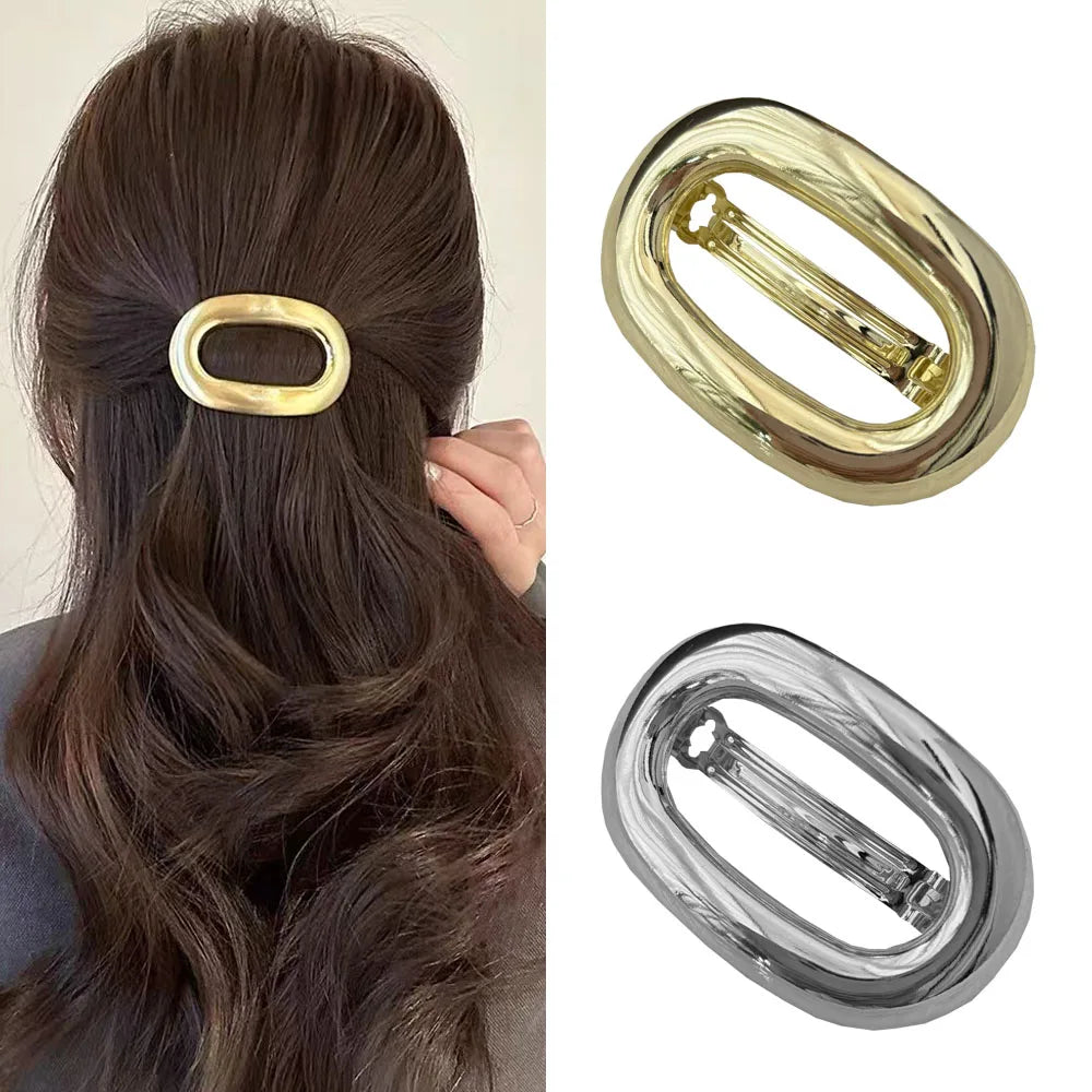 A set of elegant metal oval hair clips shown against a dark brown hair background.