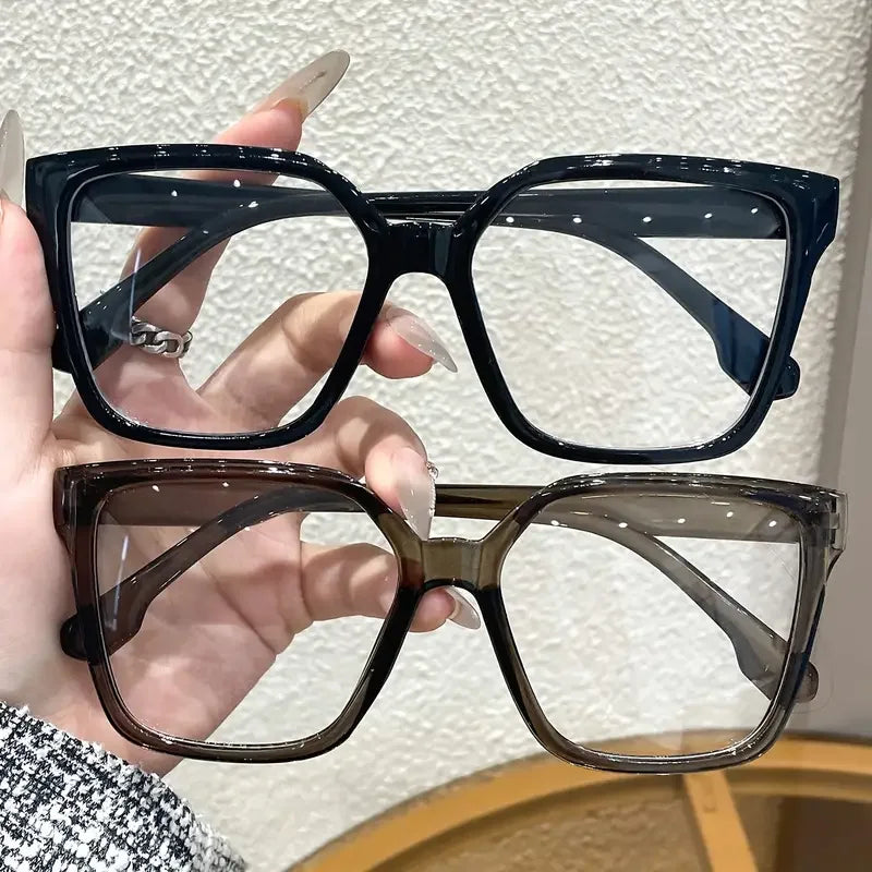 A hand holds a pair of black and brown geometric reading glasses with transparent lenses.