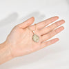 A hand holds a gold-toned classic Virgin Mary prayer pendant necklace.