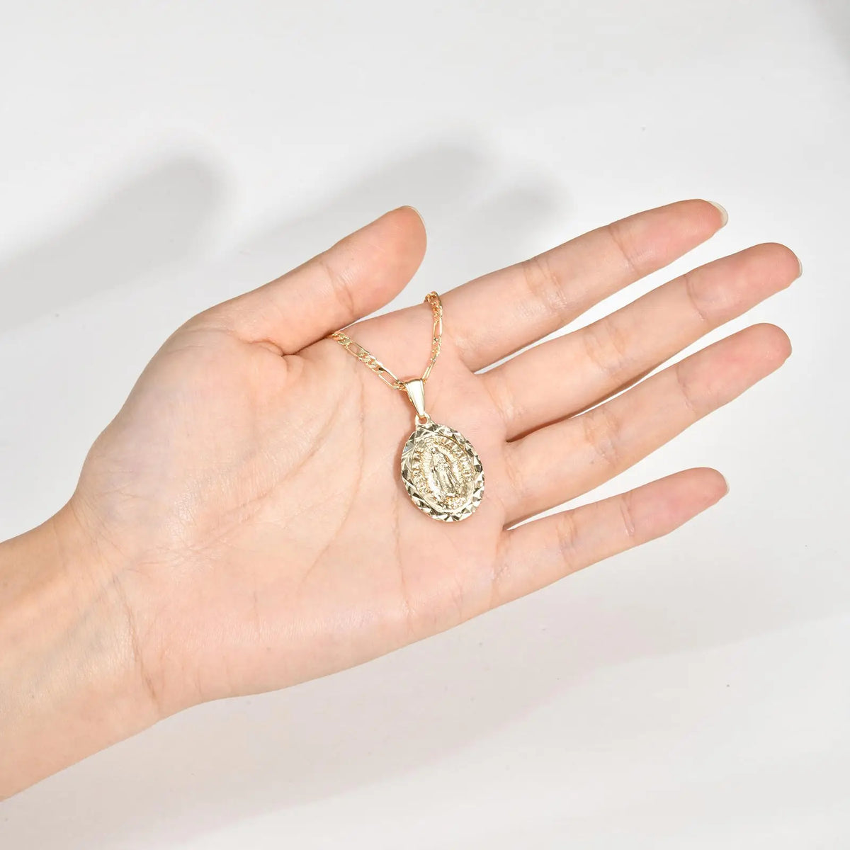 A hand holds a gold-toned classic Virgin Mary prayer pendant necklace.