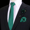 Chaqueta oscura con camisa blanca, corbata de seda verde esmeralda y prendedor floral verde a juego.