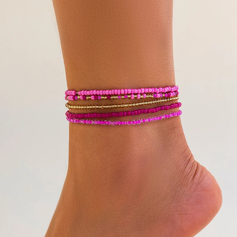 A stack of multi-layered pink and gold beaded anklets worn on a person's ankle.