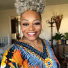A woman with short gray afro puff hair smiles while wearing a colorful patterned top.