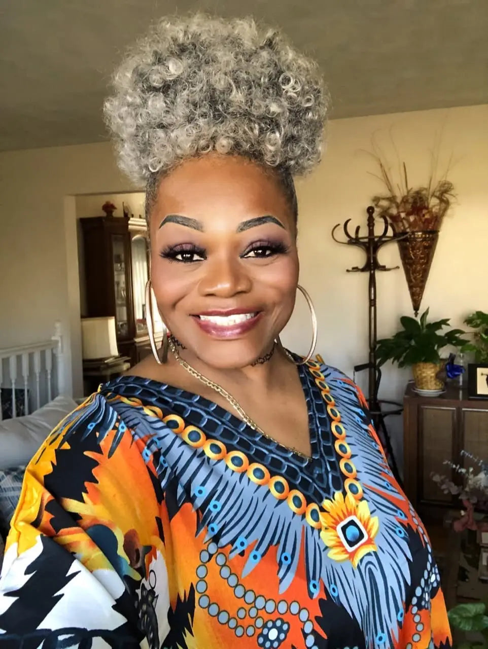 A woman with short gray afro puff hair smiles while wearing a colorful patterned top.