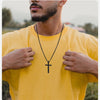 Un hombre con una camiseta amarilla muestra un collar de cruz de acero inoxidable negro.