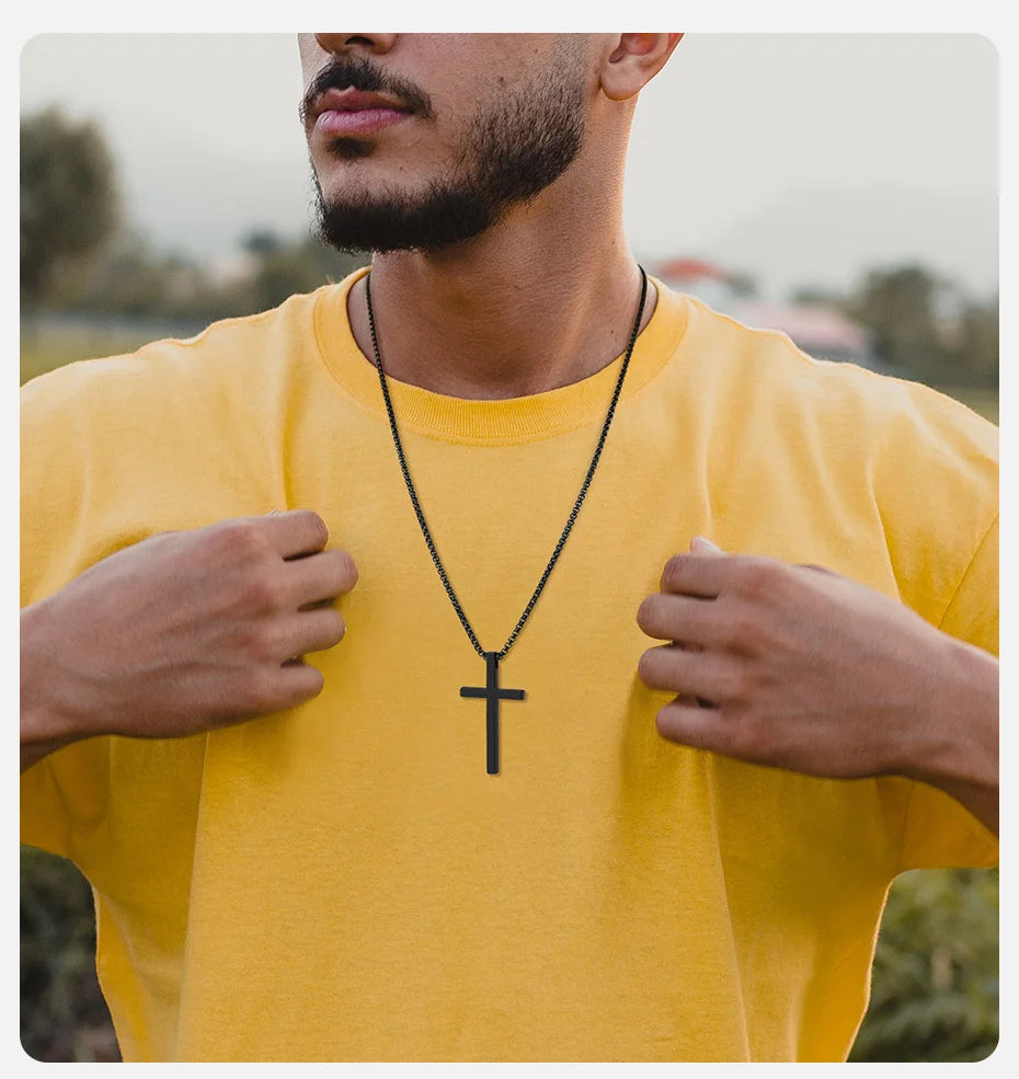 Un hombre con una camiseta amarilla muestra un collar de cruz de acero inoxidable negro.