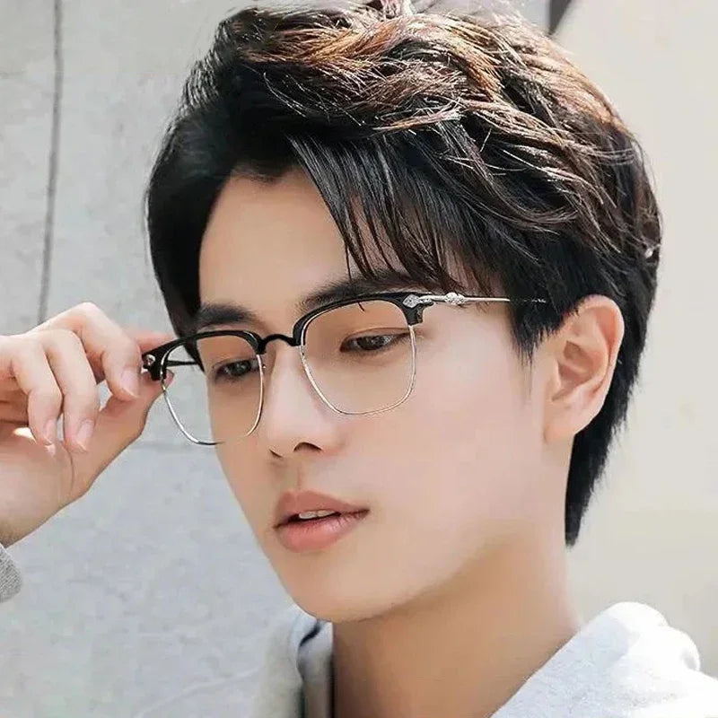 A close-up portrait of a young man wearing black metal half-frame reading glasses.