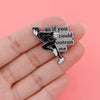 Broche en émail argenté représentant une figure en pose dynamique avec le texte : tu ne pourras pas me rattraper