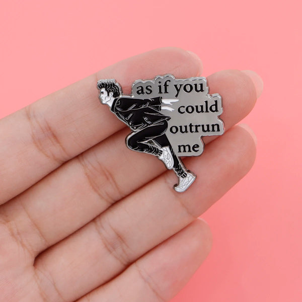 Broche de esmalte plateado que representa una figura en pose dinámica con el texto: 'como no me alcanzas'