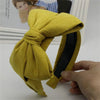 A yellow velvet wide bow headband is shown being held by a hand.