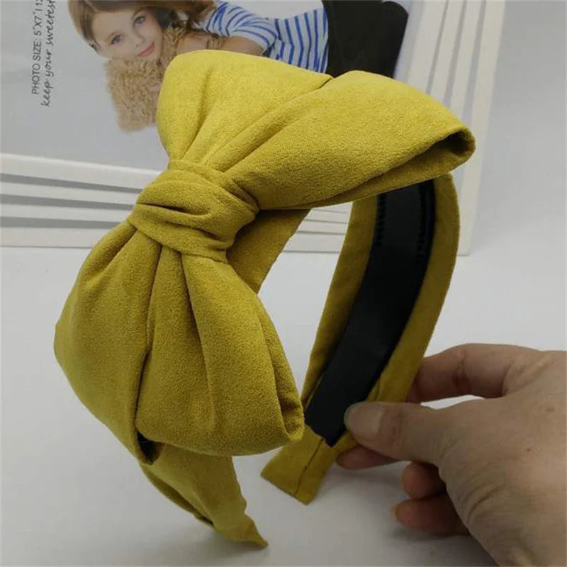 A yellow velvet wide bow headband is shown being held by a hand.