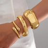 A set of three gold geometric wave bangles worn on a wrist against a light background.