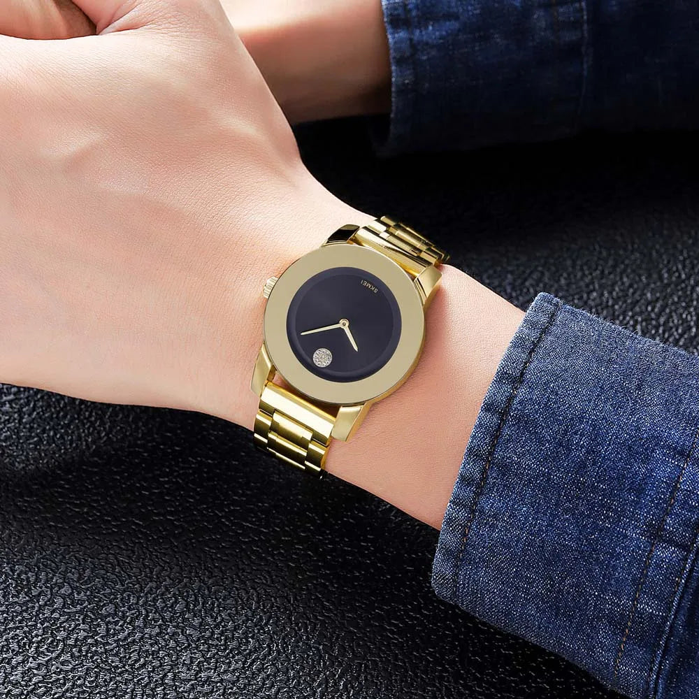 A close-up of a gold-toned minimalist quartz wristwatch worn on a wrist, resting on dark fabric.