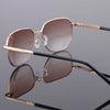 A pair of gold-toned sunglasses with rose-tinted lenses and clear bifocal inserts resting on a reflective surface.