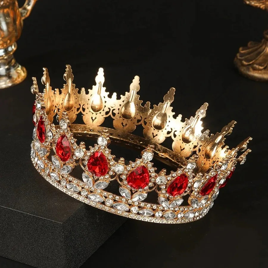 Couronne diadème en strass de cristal or avec des gemmes rouges posée sur une surface sombre.