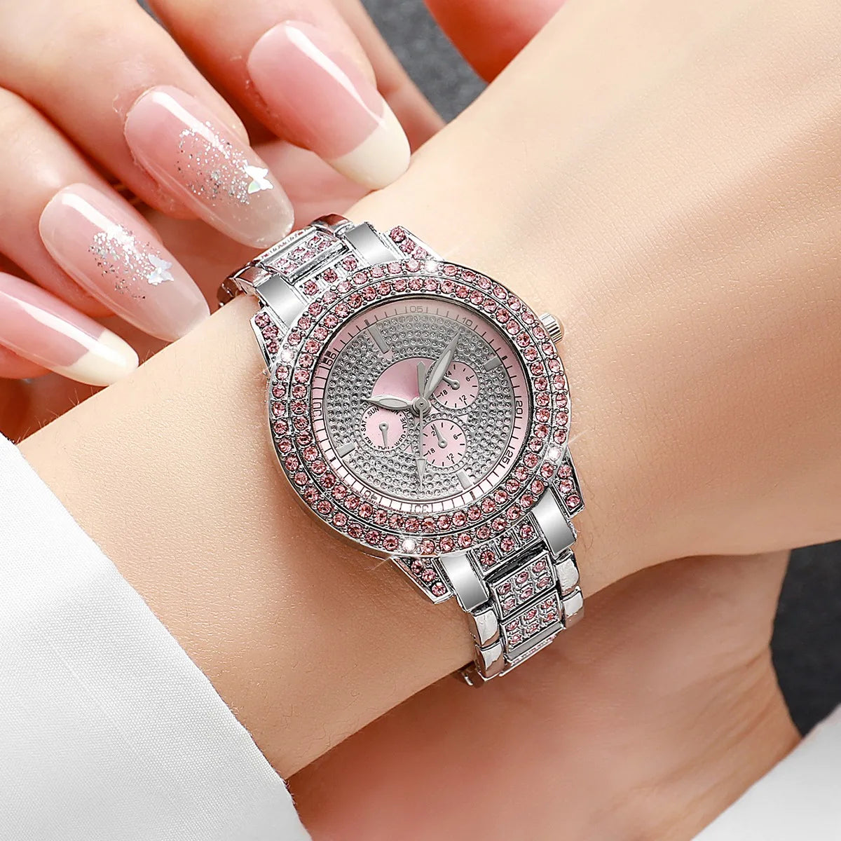 A close-up shot of a silver watch with pink accents and diamond rhinestones worn on a wrist.