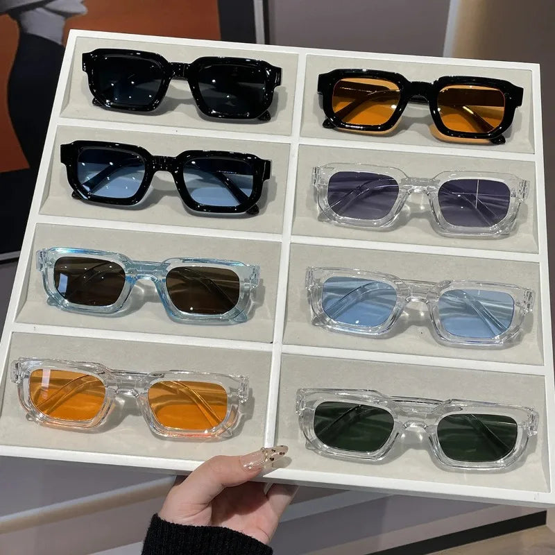 A collection of retro square fashion sunglasses in various colors and finishes displayed in a white tray.