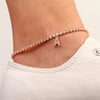 A delicate gold-toned anklet bracelet featuring small clear stones and an initial charm worn on a person's ankle.