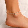 A gold-toned letter anklet bracelet with small diamonds is worn on a person's ankle.
