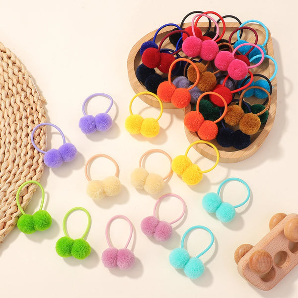 A collection of colorful double plush elastic hair bands in shades of pink, yellow, blue, and orange arranged on a wooden tra