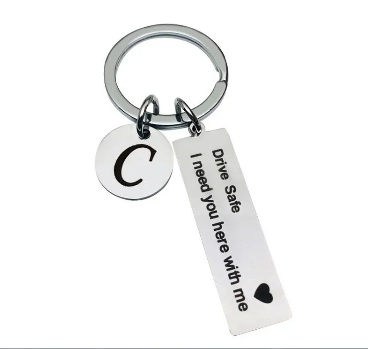 Silver keychain with a circular charm featuring the letter C and a tag that reads Drive Safe I need you here with me
