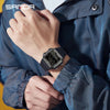 A person wearing a black digital sports watch with a metal band on their wrist, visible under a blue jacket.