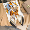 A silk scarf featuring abstract animal designs in orange, blue, and beige tones laid on a neutral background.