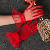 A pair of red lace tulle finger gloves are displayed against a dark gray fabric with a glass accessory.