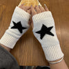 Par de guantes de dedo de punto blancos con diseños de estrella negra, sostenidos sobre una mesa de madera.
