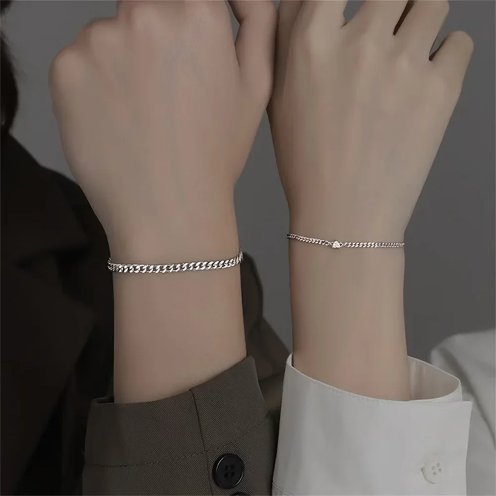 A close-up of a woman's wrist showing a set of dainty stainless steel heart link bracelets.