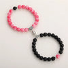 A pair of natural stone heart couple bracelets featuring pink and black beads and silver accents.