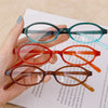 Une main tient des lunettes de mode ovales rétro Y2K dans différentes nuances de vert, rouge et brun.