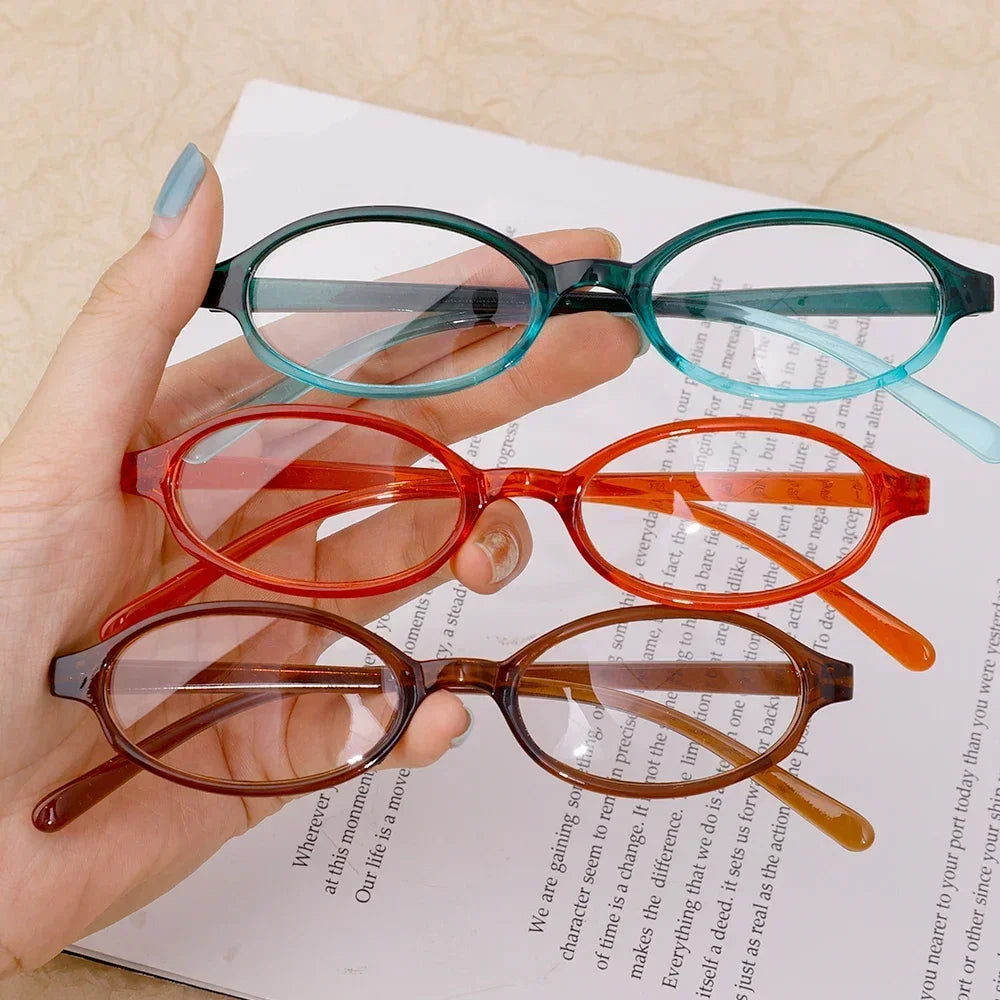 Une main tient des lunettes de mode ovales rétro Y2K dans différentes nuances de vert, rouge et brun.