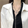 A close-up of a woman wearing a silver heart-shaped necklace under a black shirt and white jacket.